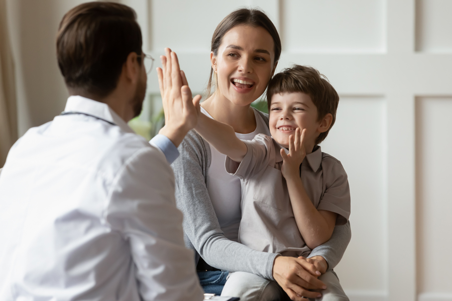 A woman and a child are seated on a couch, engaging in a conversation with their doctor.