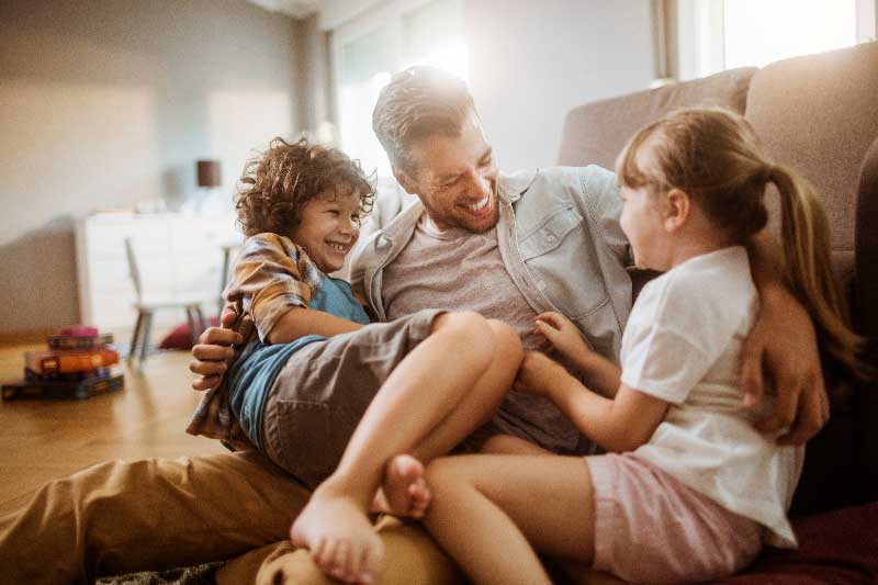 A man sits on a couch with two children, creating a warm and familial atmosphere in the living room.