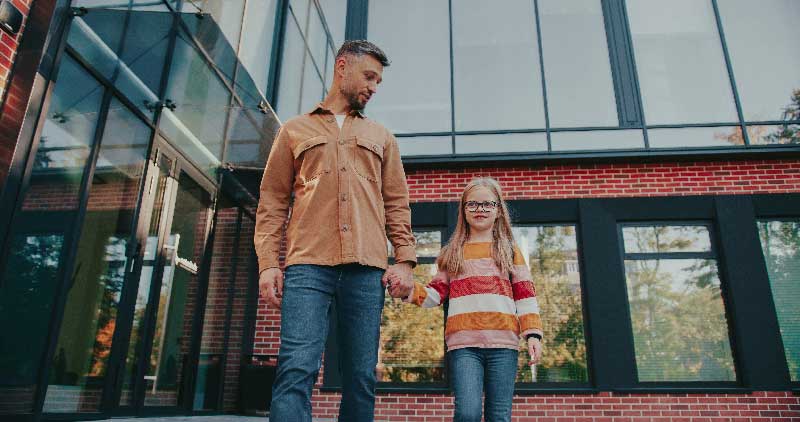 A man and a young girl stroll together outside a building, enjoying their time in the fresh air.