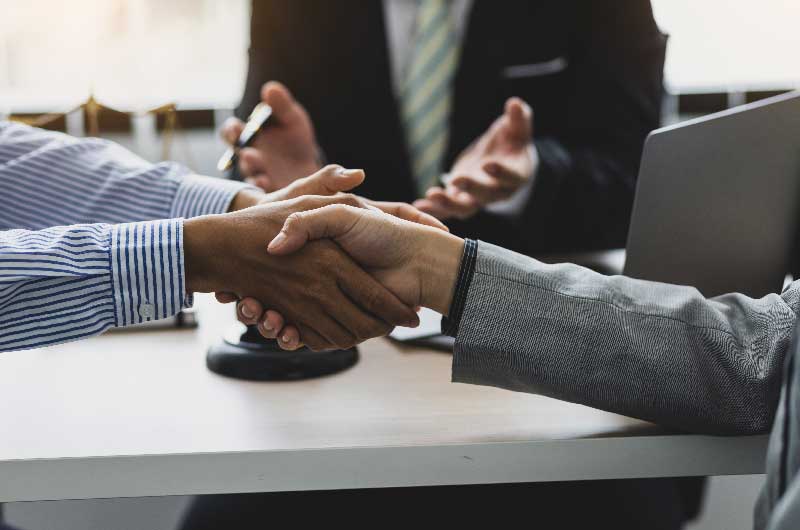 Two business professionals shaking hands over a conference table, symbolizing agreement and collaboration in a professional setting.