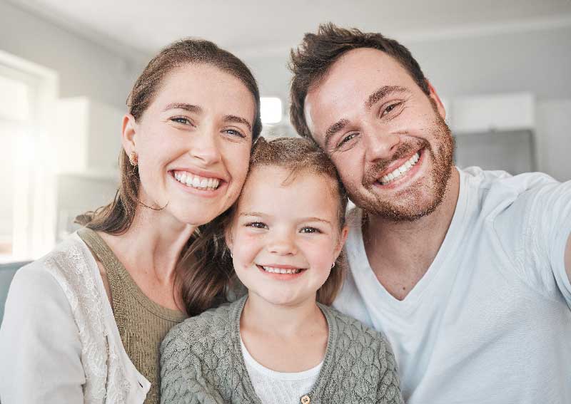 A man, woman, and child smiling together while taking a selfie, capturing a joyful family moment.