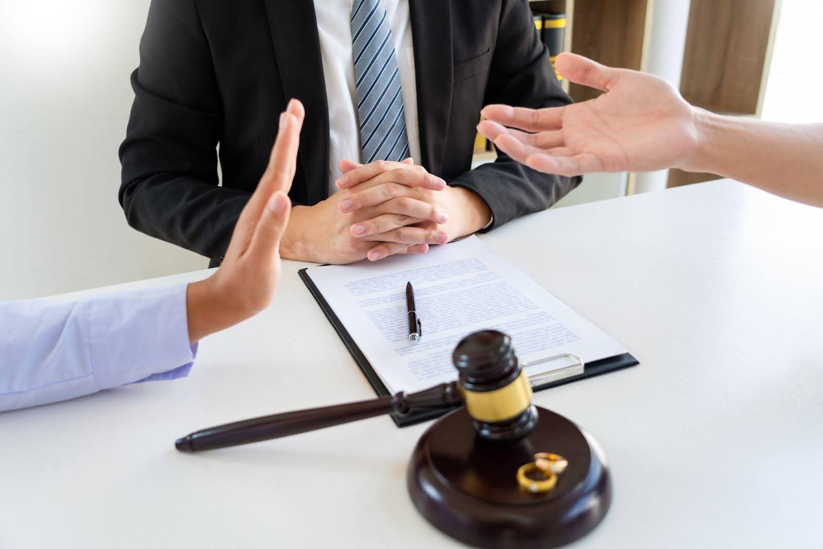 A judge speaks to two lawyers as a man holds his hand indicating emotional support in the courtroom