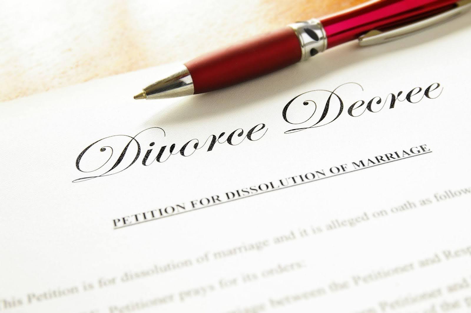 Divorce decree held in one hand with a pen beside it symbolizing the finalization of a marriage