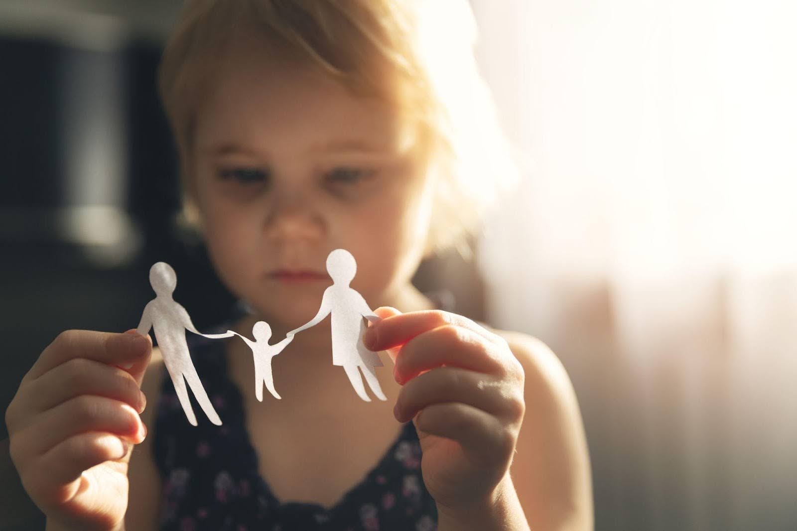 A young girl smiles while holding colorful paper cutouts representing a family