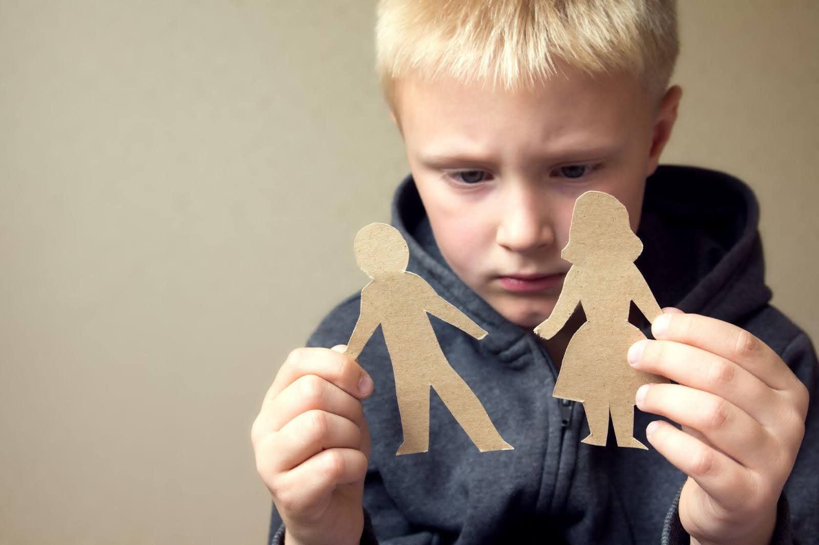 A young boy proudly holds up colorful paper cutouts representing a family smiling at the camera