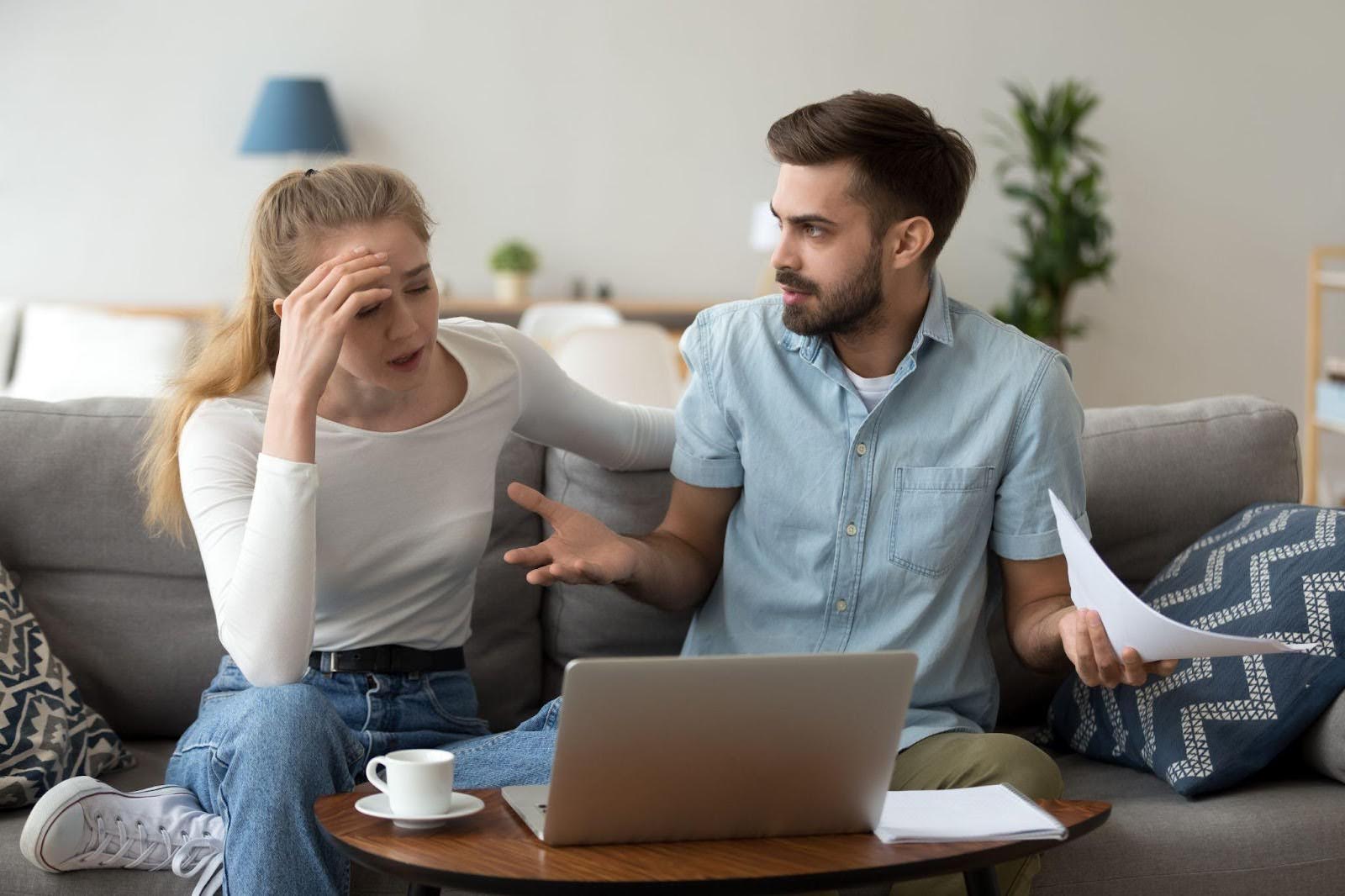 A couple sits on a couch visibly upset engaged in a heated argument
