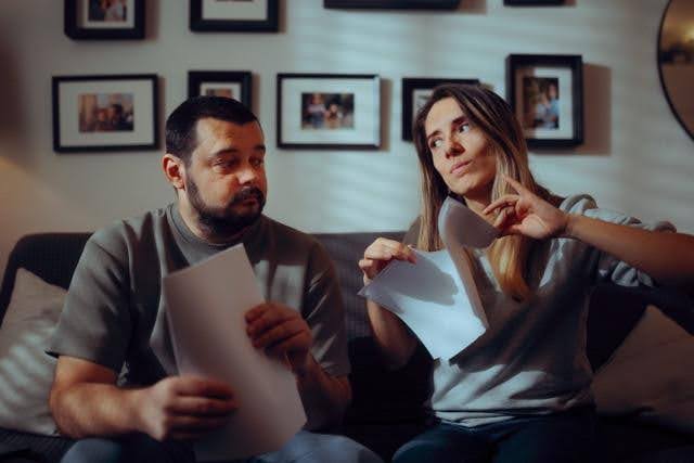 A man and woman sit on a couch reviewing documents together with focused expressions