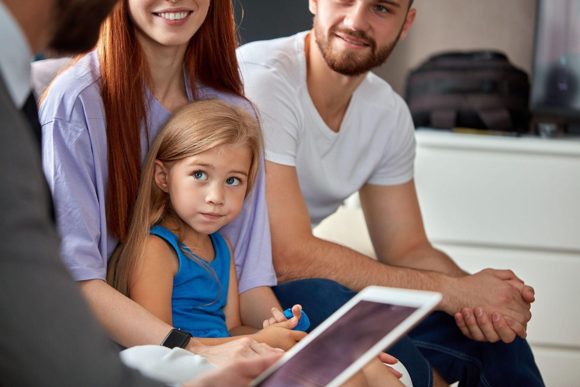 A man and woman sit on a couch with a child smiling and enjoying a cozy family moment together