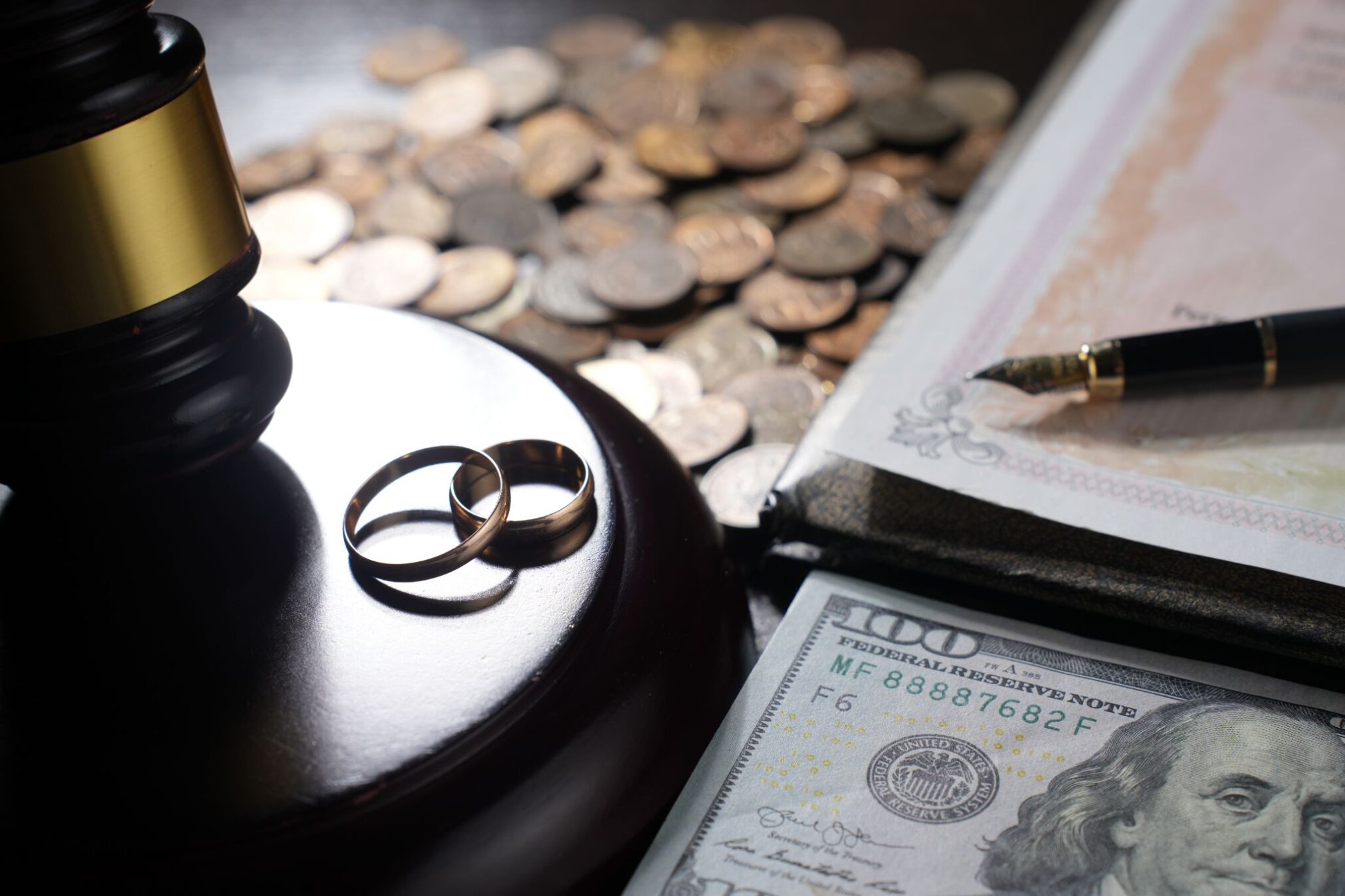 Two wedding rings on a judge's gavel next to a hundred-dollar bill and legal documents.